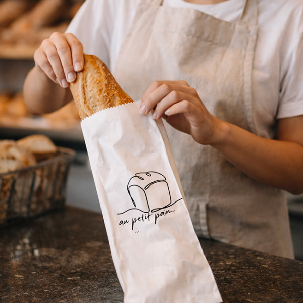 Vendeur qui emballe une baguette dans un sachet personnalisé